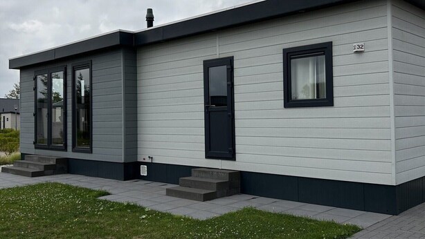 Een modern huis met twee verdiepingen, een grijze gevel, zwarte accenten en het nummer 32 aan de zijkant.
