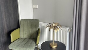 Een hoek van een kamer met een groene fauteuil, een klein rond tafeltje met een gouden voet en een decoratieve plant.