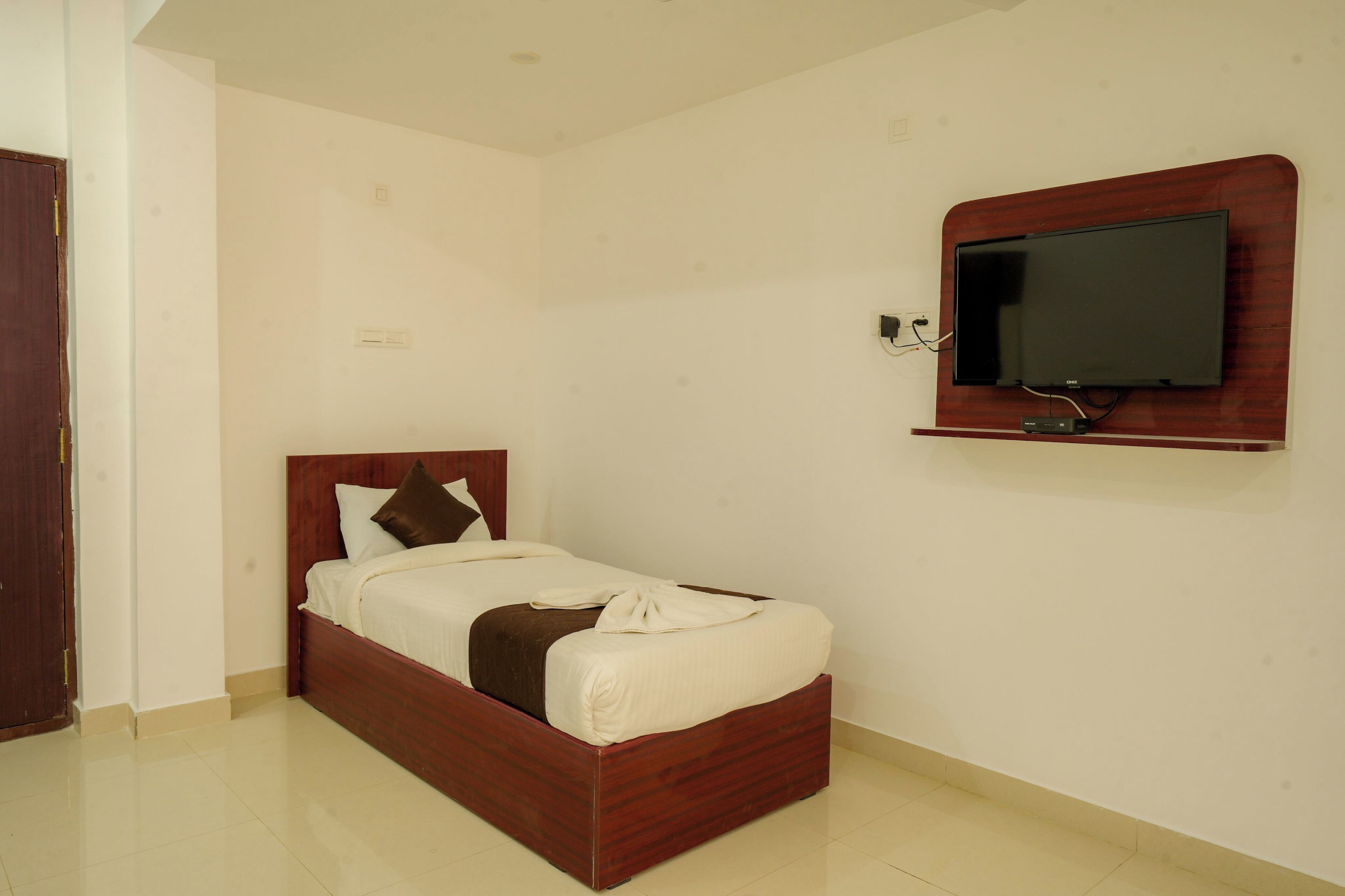 A single bed with a wooden frame, a television mounted on the wall, and a door to the left.