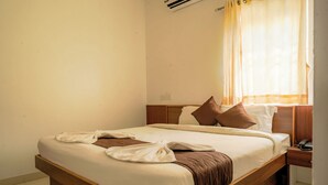 A neatly made bed with pillows, a bedside table with a phone, and a window with curtains. - JR Service Apartment  (Coimbatore)