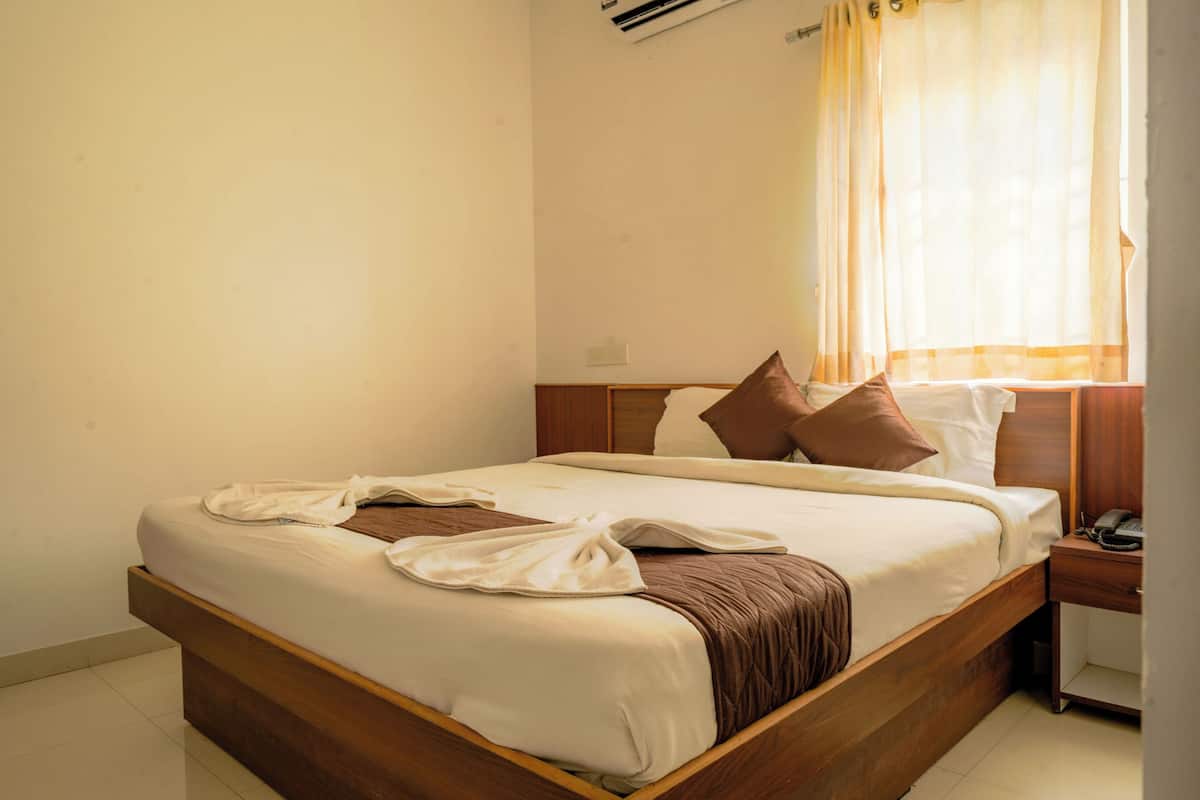 A neatly made bed with pillows, a bedside table with a phone, and a window with curtains.