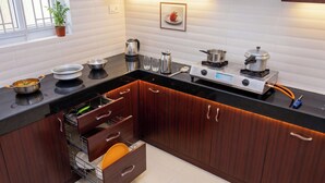 A modern kitchen with wooden cabinets, a black countertop, and various kitchen appliances. - JR Service Apartment  (Coimbatore)