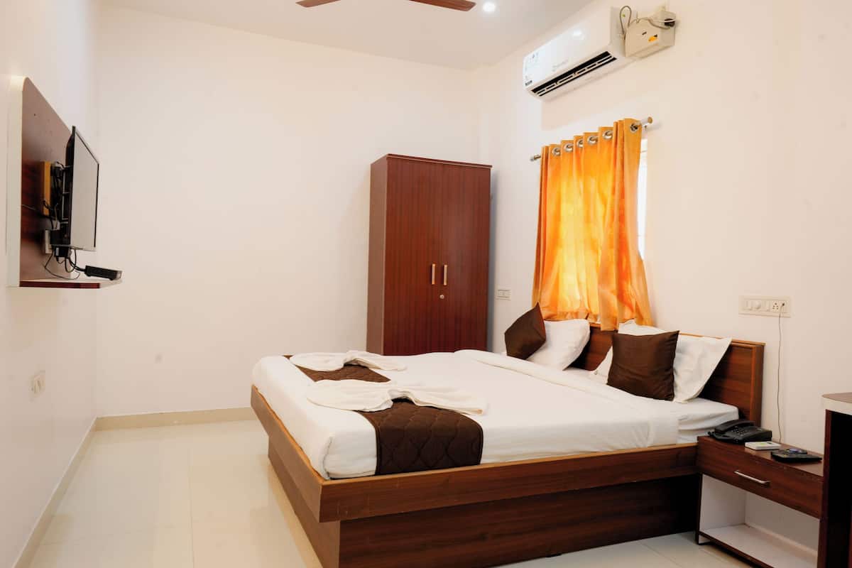 A bedroom with a bed, a wardrobe, a bedside table, a TV, and an air conditioning unit.