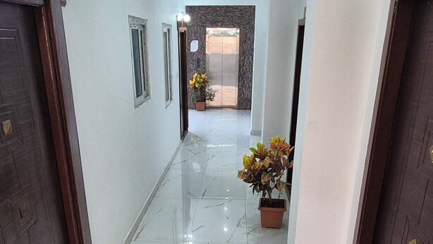 A hallway with marble flooring, wooden doors, and a potted plant. - JR Service Apartment  (Coimbatore)