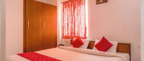 A bedroom with a bed, a wooden wardrobe, a red curtain, and a small picture on the wall.