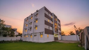 A multi-story residential building with a flat roof, multiple balconies, and a well-maintained lawn in the foreground. - JR Service Apartment  (Coimbatore)