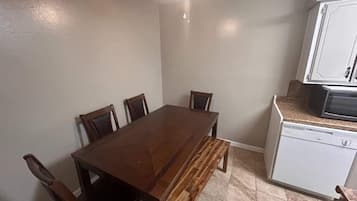 Un coin repas comprenant une table en bois et quatre chaises, un banc, ainsi qu’une cuisine équipée d’un four à micro-ondes et d’un lave-vaisselle.