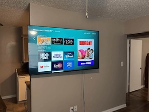 A flat-screen TV mounted on a wall displaying a streaming service interface with various content options. - Bright & Cozy 1BR Apartment by Fort Sill (Lawton)