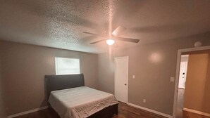 Una camera da letto con un letto, una ventola a soffitto, una finestra e una porta.