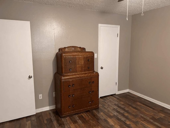 Une pièce avec une commode en bois adossée à un mur, une porte blanche et un plancher en bois.