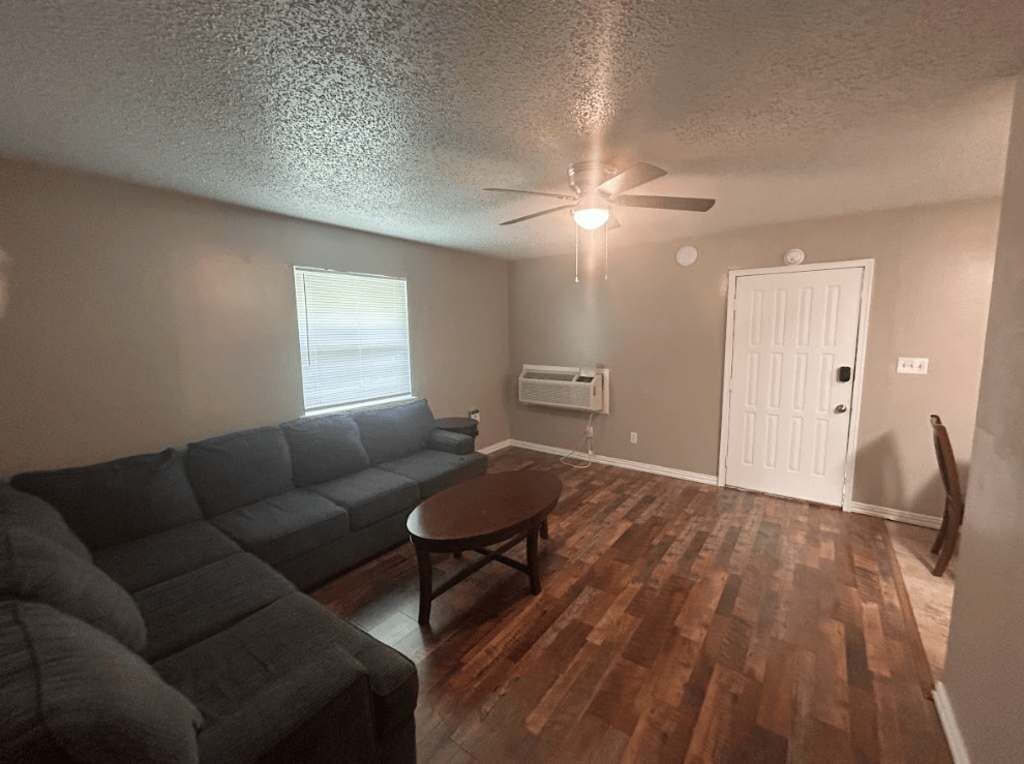 A living room with a sectional sofa, a coffee table, a ceiling fan, and hardwood flooring.
