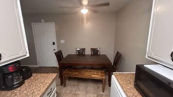 A compact kitchen with a dining table, chairs, a bench, and a microwave.