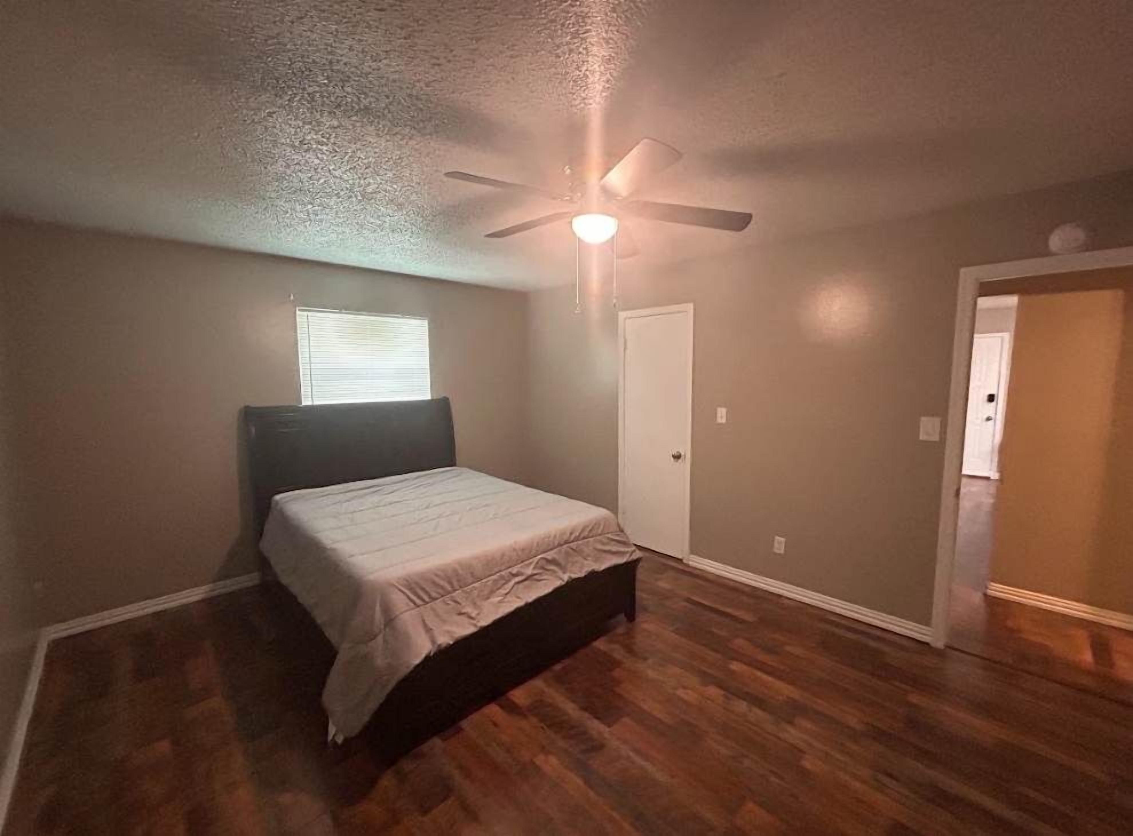 A bedroom with a bed, a ceiling fan, a door, and a window.