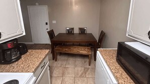 Una cucina compatta con un tavolo da pranzo, sedie, una panca, una macchina del caffè e un forno a microonde.
