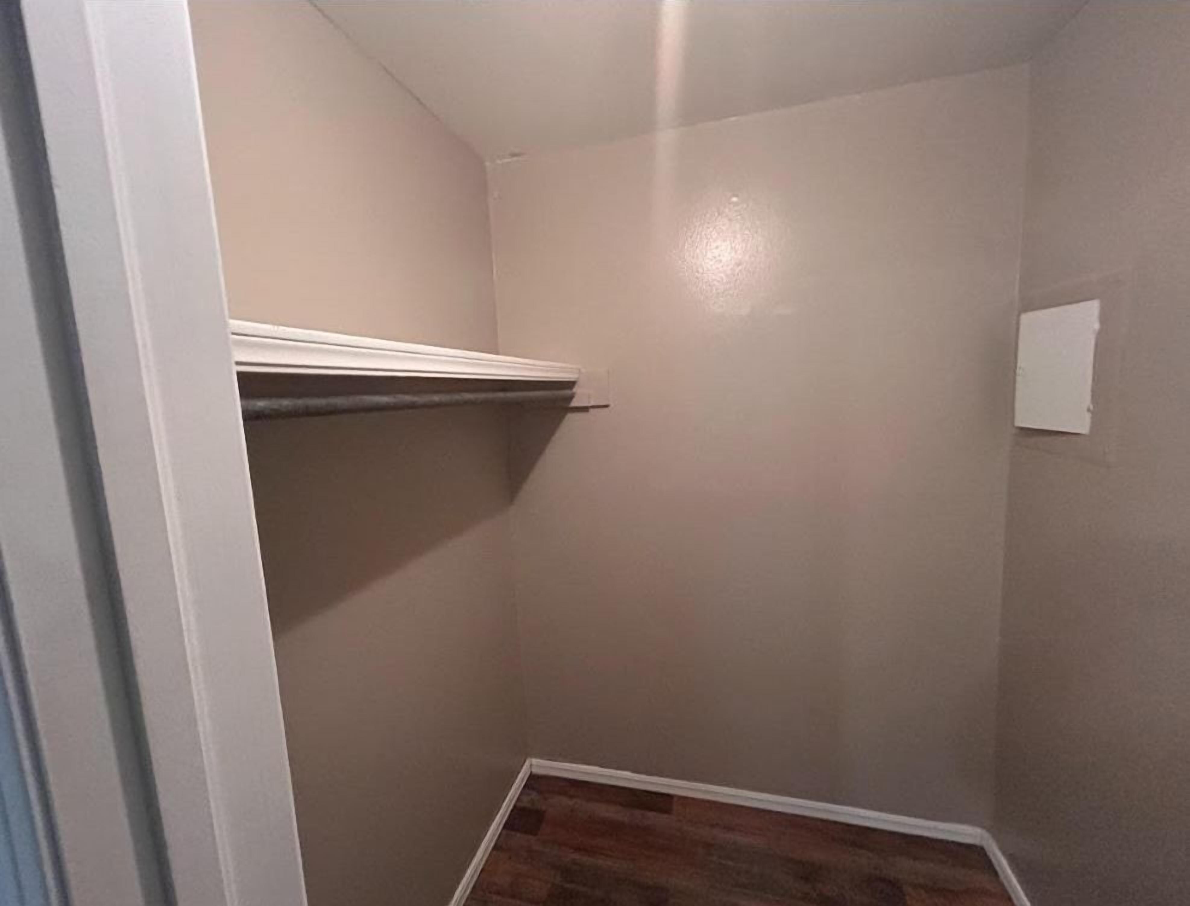 A small, enclosed room with a sloped ceiling, a wooden floor, and a white door.