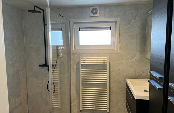 A modern bathroom with a glass shower enclosure, a built-in window, a towel rack, and a sink.