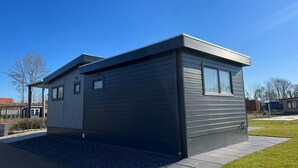 Ein modernes, eingeschossiges Haus mit dunkler Außenfassade, einer überdachten Veranda und einer kleinen angebauten Garage.