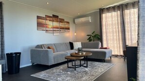 Ein modernes Wohnzimmer mit einem grauen Sofa, einem Couchtisch und einem großen Fenster mit Vorhängen.
