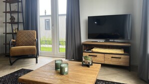 Una sala de estar con un sillón de cuero marrón, una mesa de centro de madera, un televisor sobre un mueble de madera y un ventanal corredizo que da a un balcón.