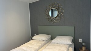 Un dormitorio con cama, un espejo en la pared y una mesita de noche con lámpara.