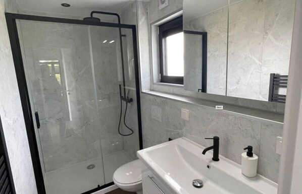 Une salle de bain moderne avec une douche en verre, des toilettes et un lavabo avec un miroir au-dessus.