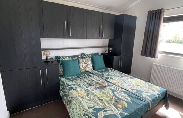 Un dormitorio con cama, armarios oscuros, una mesita de noche y una ventana con cortinas.