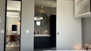 Een moderne hotelkamer met een bed, een bureau, een stoel, een spiegel en een badkamer met een wastafel en spiegel.