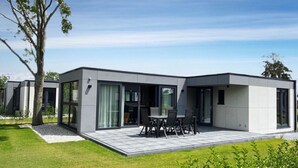 Een modern huis met een terras, grote ramen en een gazon.