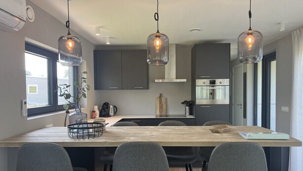 Een moderne keuken met een centraal eiland, donkere kastjes en hanglampen.
