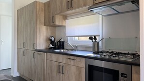 A modern kitchen with wooden cabinets, a gas stove, a coffee maker, and a window above the sink.