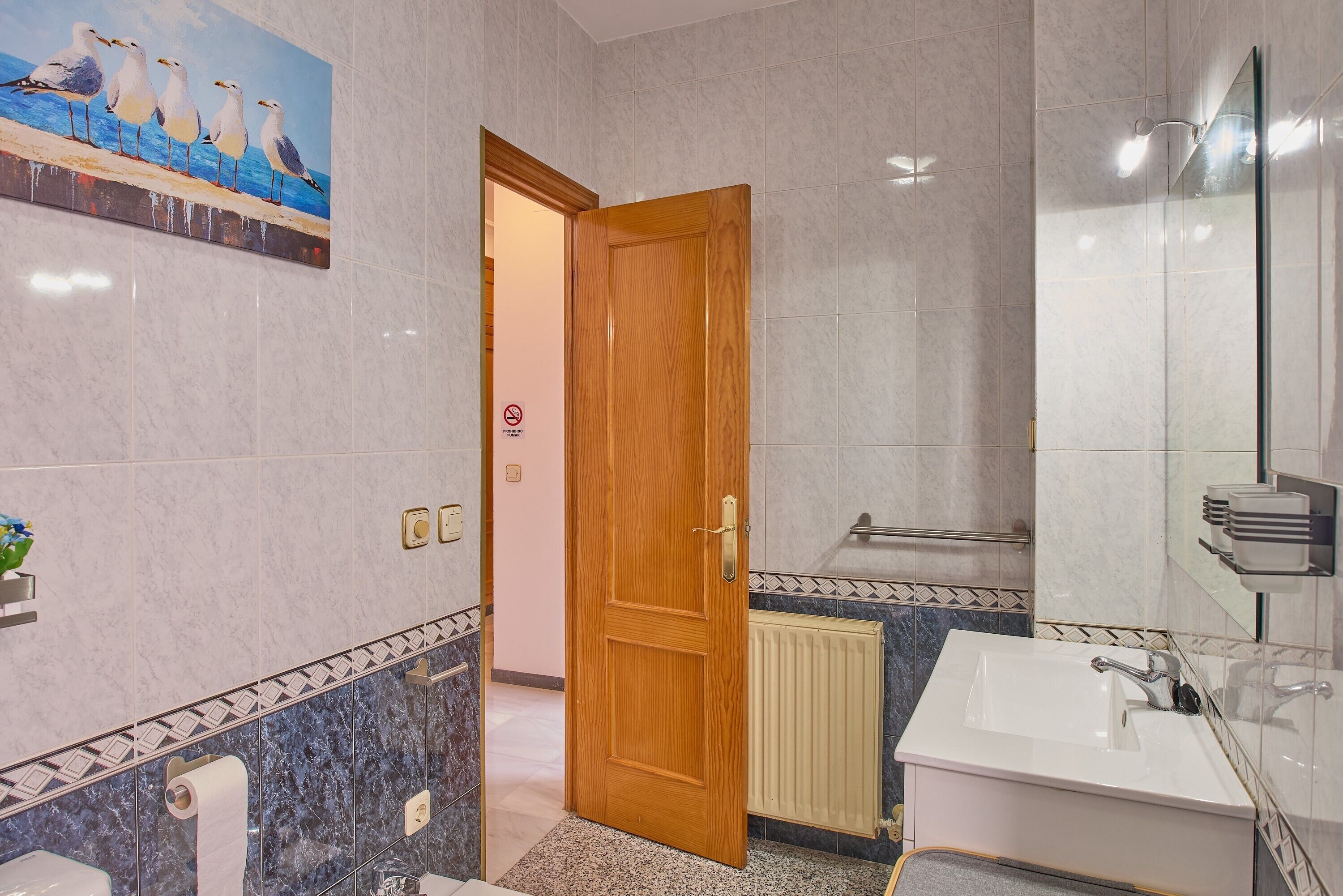 A bathroom with a wooden door, a white sink, a mirror, and a seagull painting on the wall.