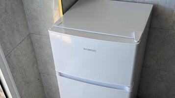 Ein weißer Kühlschrank mit dem Markennamen 'FANTON' in einer Ecke eines Raumes mit gefliesten Wänden und einer sichtbaren Tür.