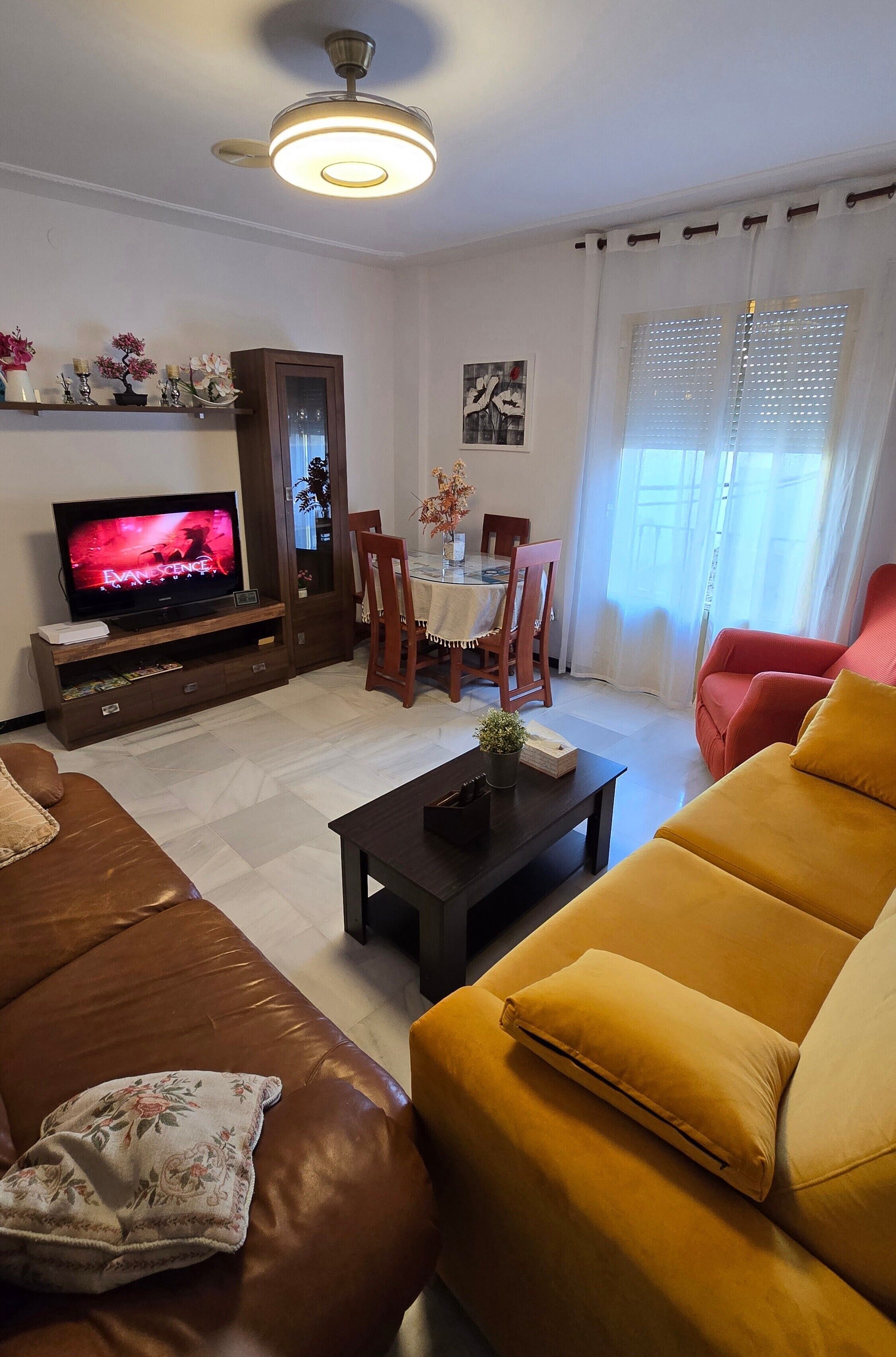 Een woonkamer met een televisie, bank, salontafel en een eethoek.