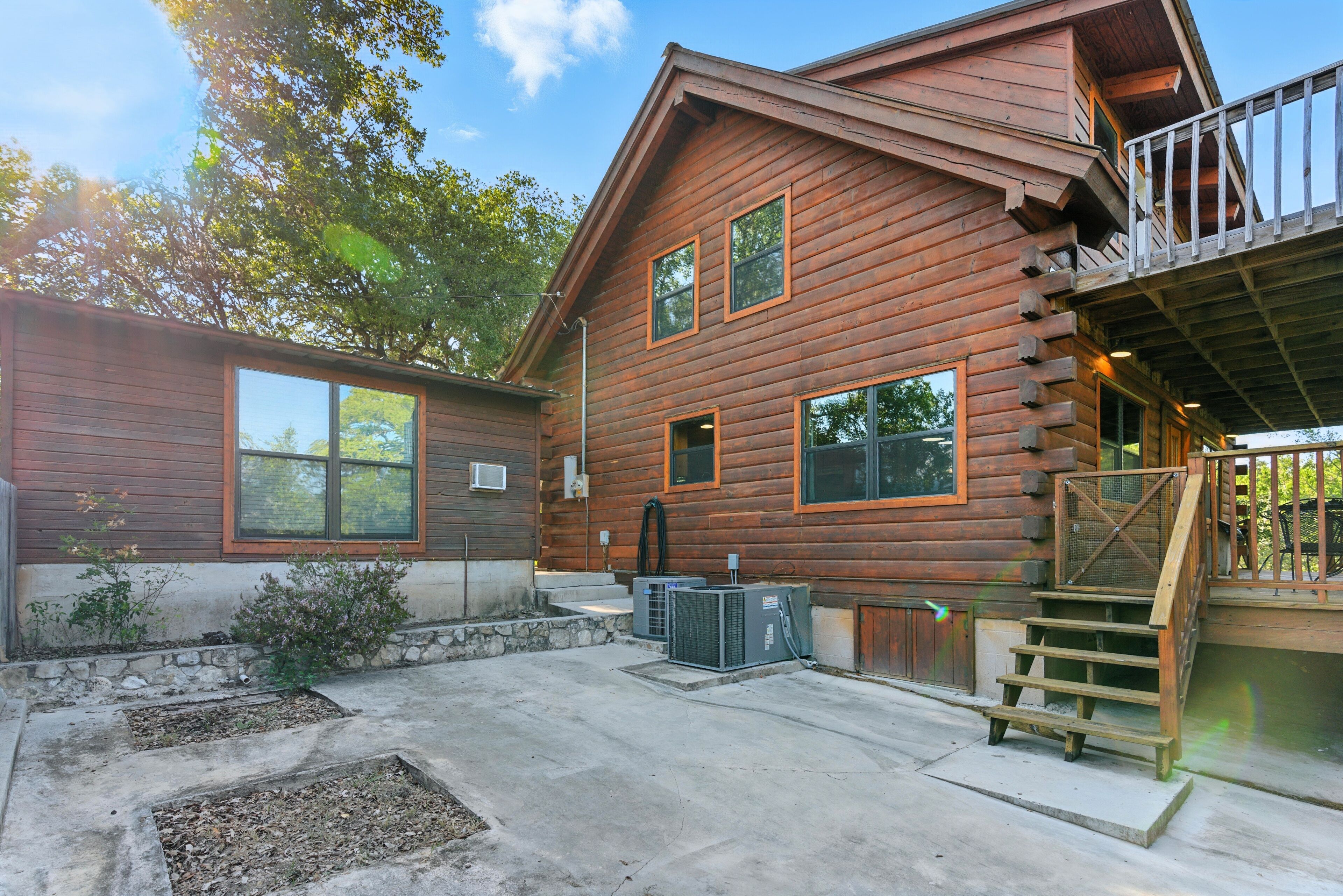 A log cabin with a balcony, a stone foundation, and a concrete patio.