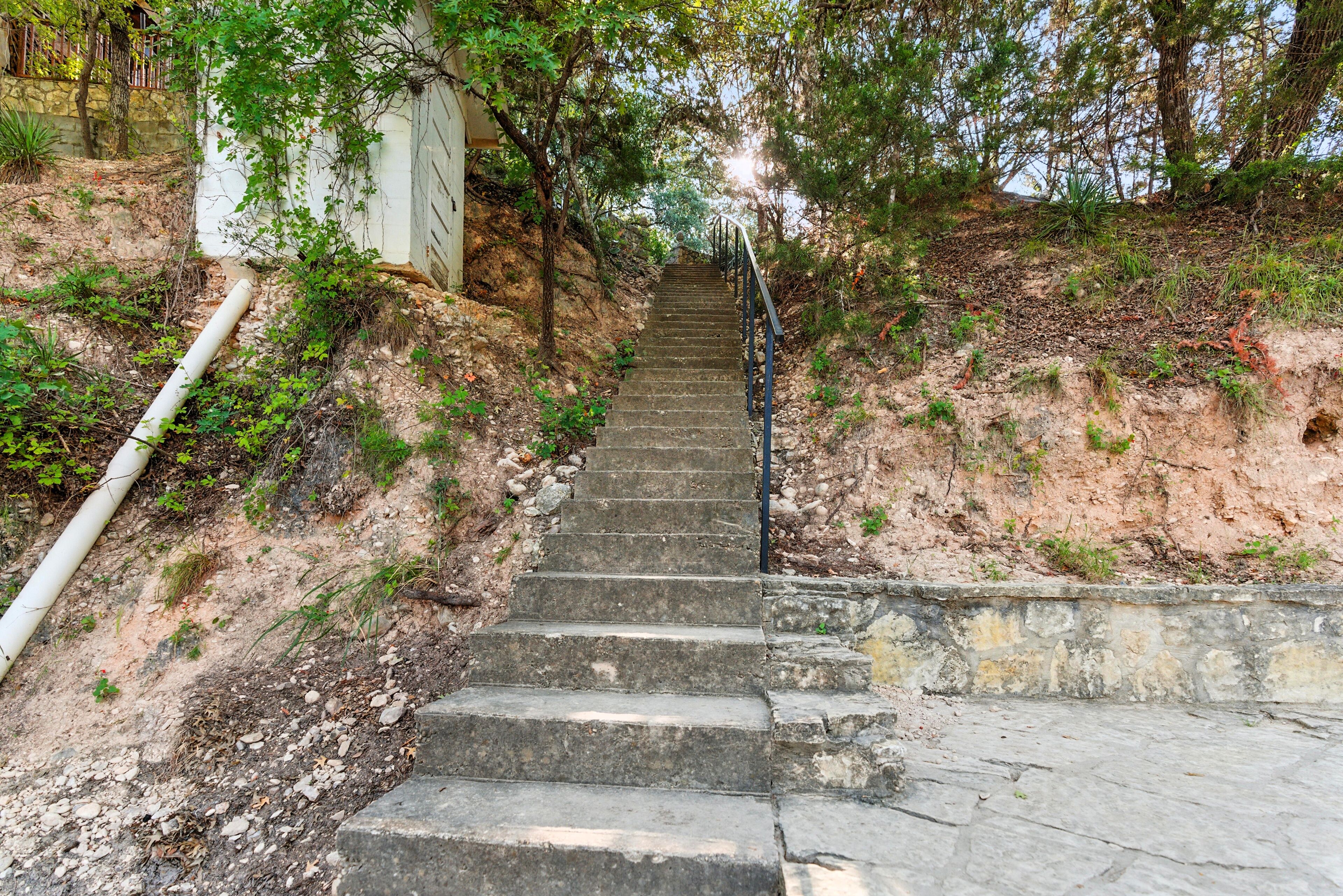 A stone staircase leading uphill with a metal railing, surrounded by trees and vegetation.