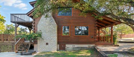 A log cabin with a stone chimney, wooden deck, and a covered porch.