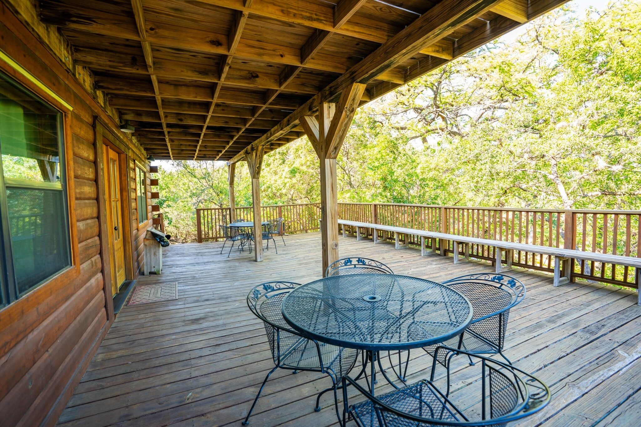 Une terrasse en bois dotée d’un espace abrité, comprenant une table et des chaises, et offrant une vue sur les arbres en arrière-plan.