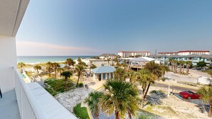 Een hotel aan het strand met uitzicht op de oceaan, palmbomen en een parkeerplaats met een rode auto.