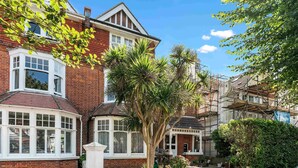 A Victorian-style house with a bay window, a conservatory, and a garden with palm trees.