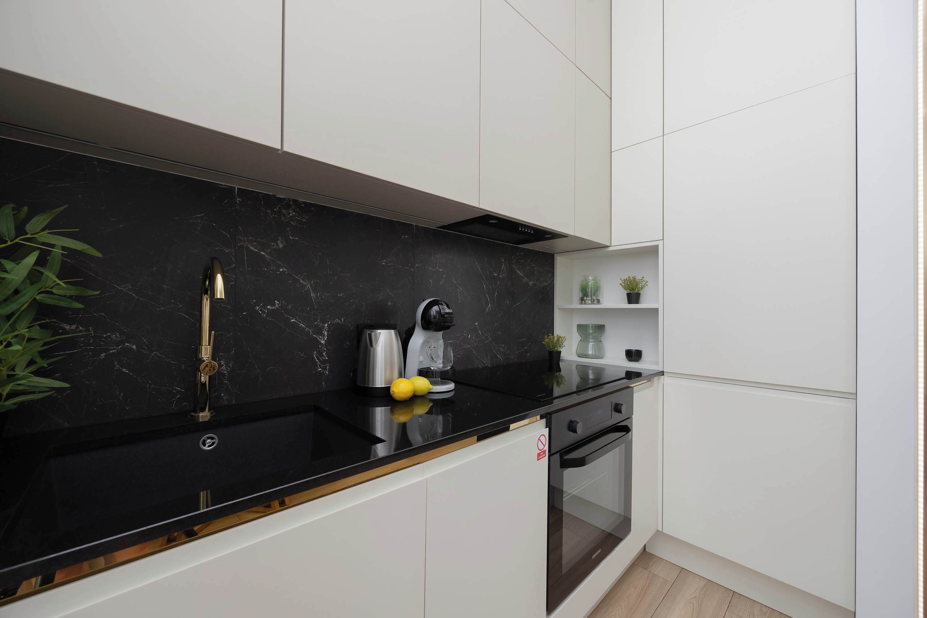 Une cuisine moderne dotée d’un plan de travail en marbre noir, de meubles blancs et d’un four encastré.