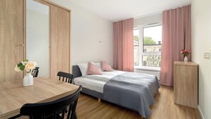 Ein Schlafzimmer mit einem Bett, einem Holztisch, einem Stuhl, einem Nachttisch und einem Fenster mit Vorhängen.