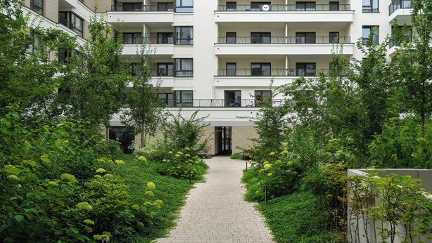 Ein Weg führt zu einem mehrstöckigen Gebäude mit Balkonen, umgeben von üppiger Vegetation.