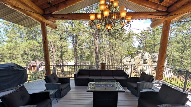Une terrasse extérieure dotée d’un plafond en bois, d’un lustre, de meubles en osier et offrant une vue sur les arbres et les rochers.
