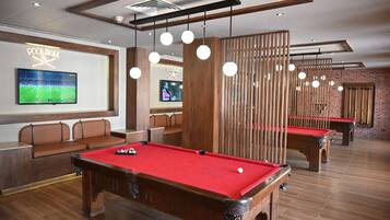 Un salón de billar con múltiples mesas de billar, bancos de madera e iluminación colgante.