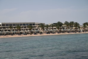 Et hotel ved stranden med flere etager, palmer og strandparasoller.
