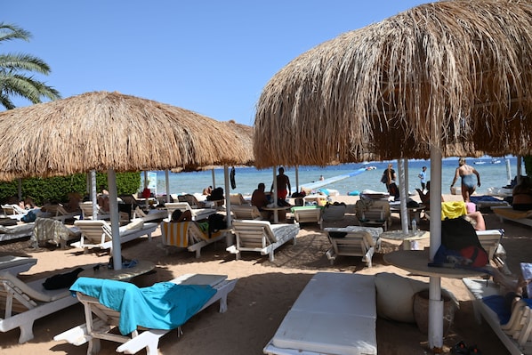 A beachside lounge area with thatched umbrellas, sun loungers, and a view of the sea.