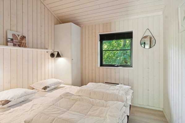 Ein Schlafzimmer mit zwei Betten, einem Fenster mit Blick auf Grünflächen, einem hängenden Spiegel und einem Regal mit einem Buch.