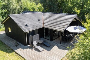 Ein modernes Haus mit geneigtem Dach, einer Terrasse mit Gartenmöbeln und einem großen Sonnenschirm.