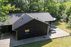 Ein modernes Gebäude mit geneigtem Dach, einer Holzterrasse und einem kleinen Fenster.