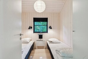 A room with two beds, a window with blinds, a ceiling light, and a wall-mounted TV.